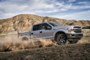 side view of a silver 2018 Ford F-150 driving up a sandy hill