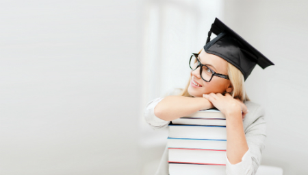 young woman in graduation cap resting head on stack of textbooks