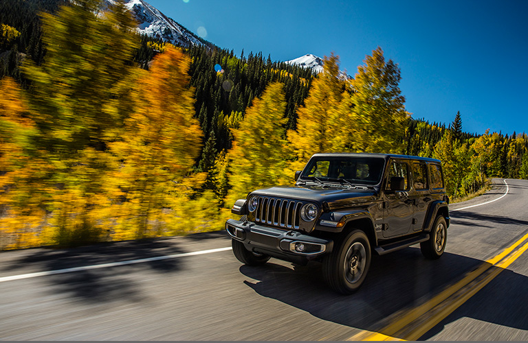 2018 Jeep Wrangler driving on mountainous road with trees lining pavement
