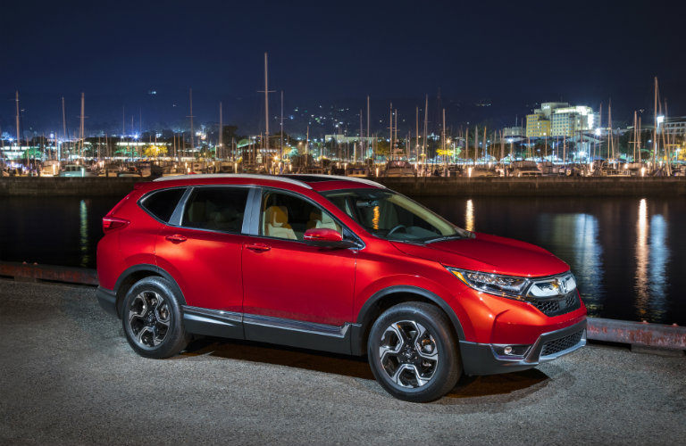 Red Honda CR-V parked in front of harbor with city in background