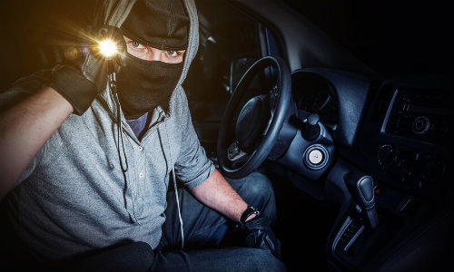 Man wearing a mask and holding up flashlight inside car to see