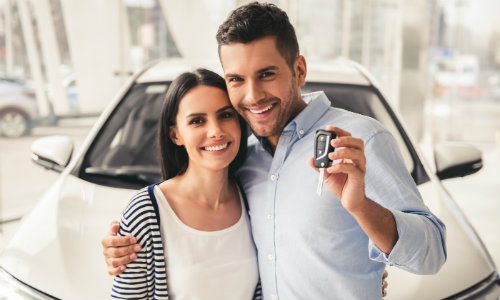Couple posing in front of a car with keys in the man's hand