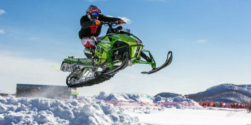 Man jumping a snowmobile over snow bank