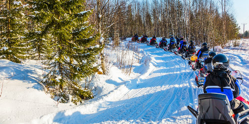 Large group of snowmobiling tourists heading down winter trail