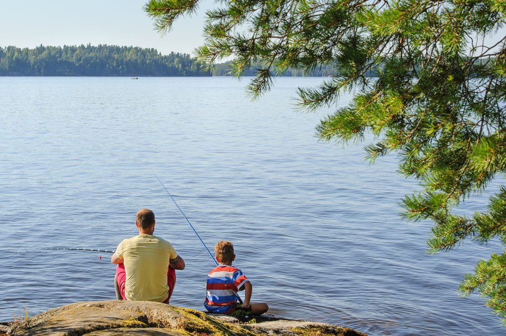 Father and son sitting by the water fishing on a rock. 
