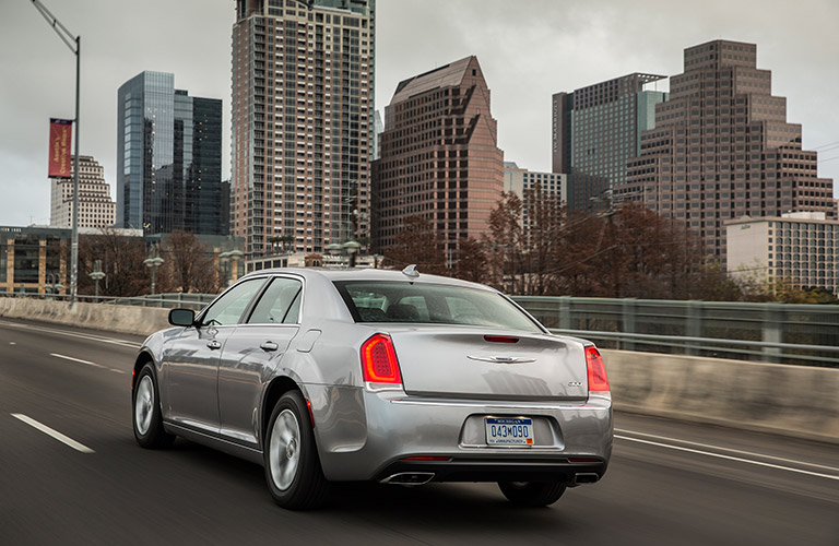 Rear view of silver 2018 Chrysler 300 driving with city skyline in background