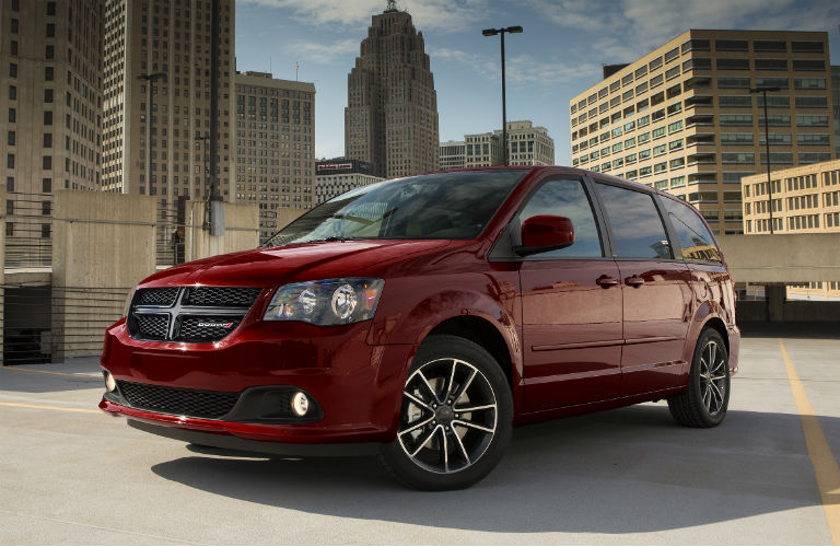 Red Dodge Grand Caravan parked in front of city skyline