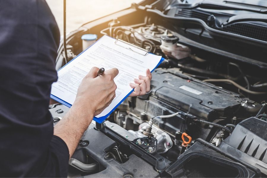 Mechanic checking off items on a list while inspecting engine