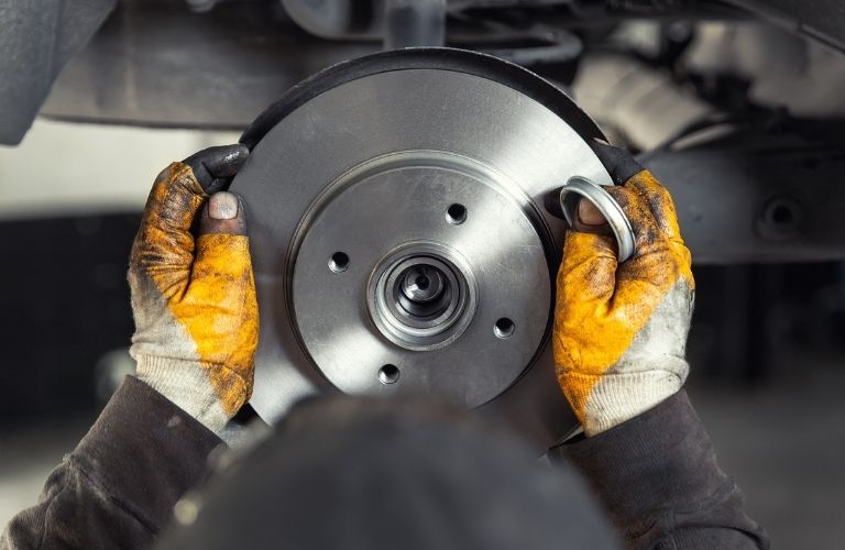 Closeup male tehnician mechanic greasy hands in gloves install new car oem brake steel rotor disk during service at automotive workshop auto center