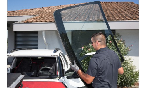 Man replacing windshield carrying it outside family home with brown tile roof