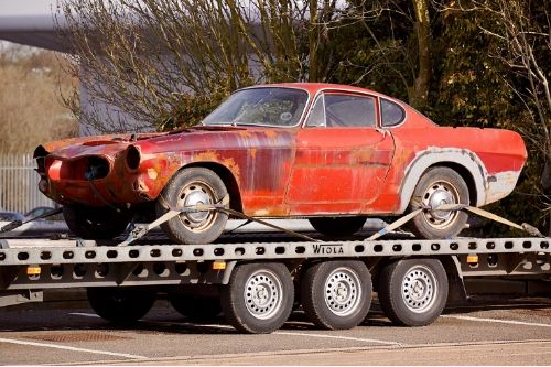 An old car resides atop a trailer that hauls it.