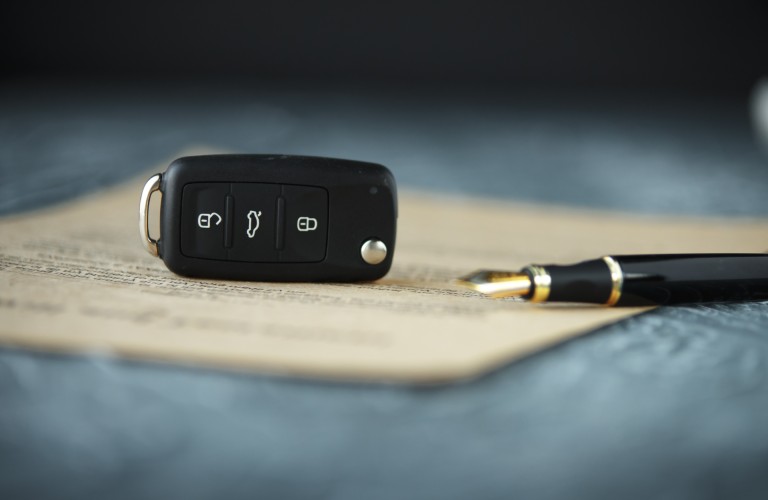 A set of car keys lying next to paperwork and an ink pen on a table.