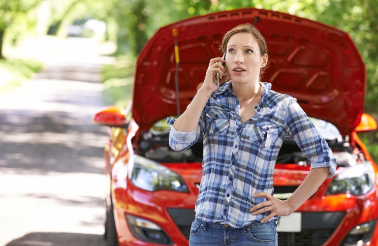 A redheaded woman standing in front of her vehicle calling for help.