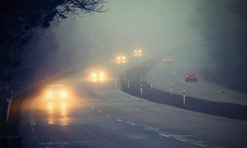foggy and rainy road with car driving with headlights on