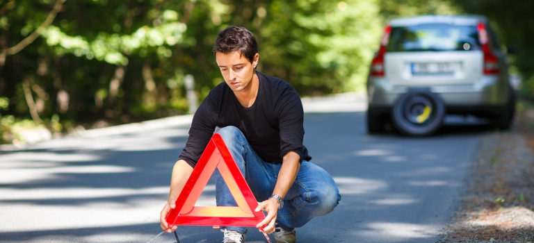 Person placing a roadside warning sign behind a broke down car