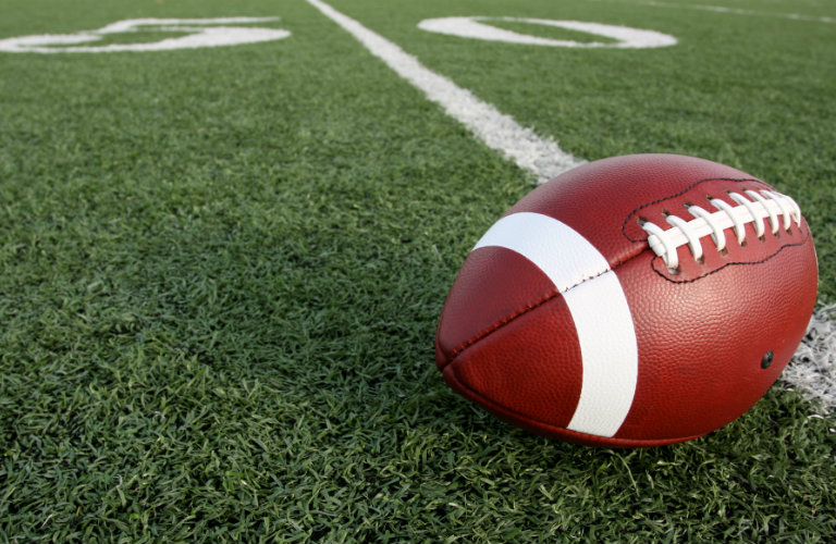 brown football laying on 50 yard line of football field