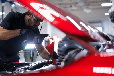 Mazda technician pouring oil into engine using funnel