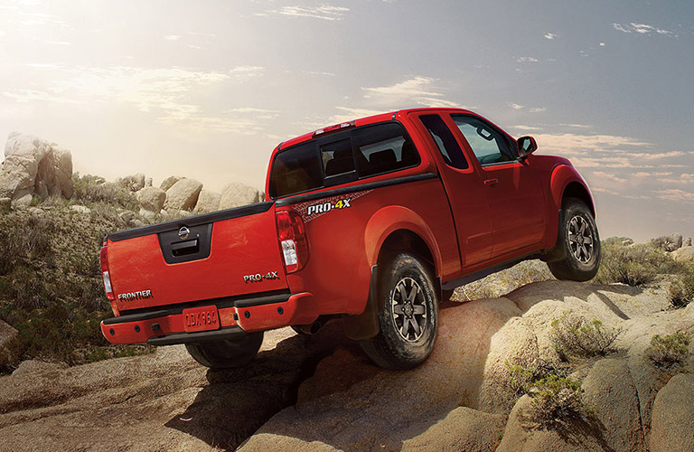 Rear view of red 2018 Nissan Frontier pickup scaling up rocky hill