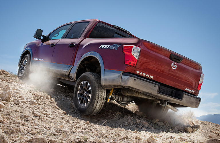 Rear view of red 2018 Nissan TITAN pickup driving up gravelly hill