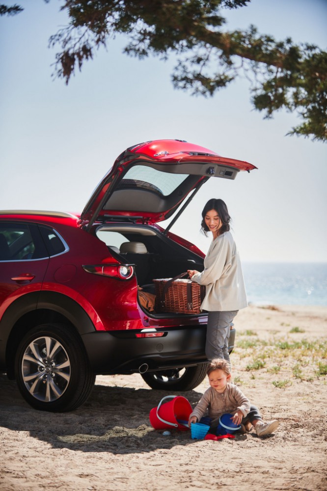 rear of a red 2021 Mazda CX-30 with cargo door open, woman looking inside and young child playing