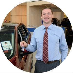 Smiling man with tie holding key in front of new Ford model